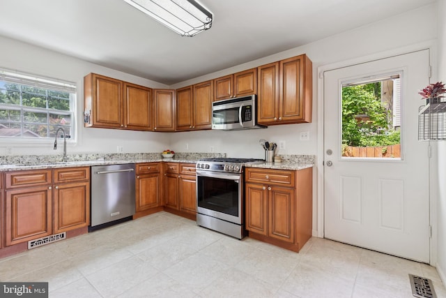 6311 Gentele Ct, Alexandria, VA 22310 - kitchen featuring appliances with stainless steel finishes, brown cabinets, plenty of natural light, and light stone countertops
