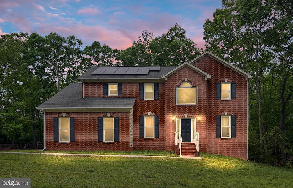 view of front of home with roof mounted solar panels, brick siding, a front lawn, and entry steps