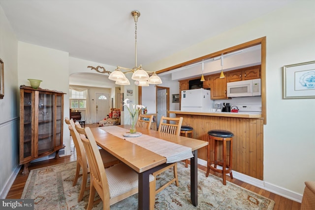dining space featuring arched walkways, baseboards, and light wood-style floors