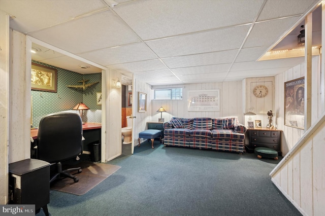 carpeted home office featuring a drop ceiling and wooden walls