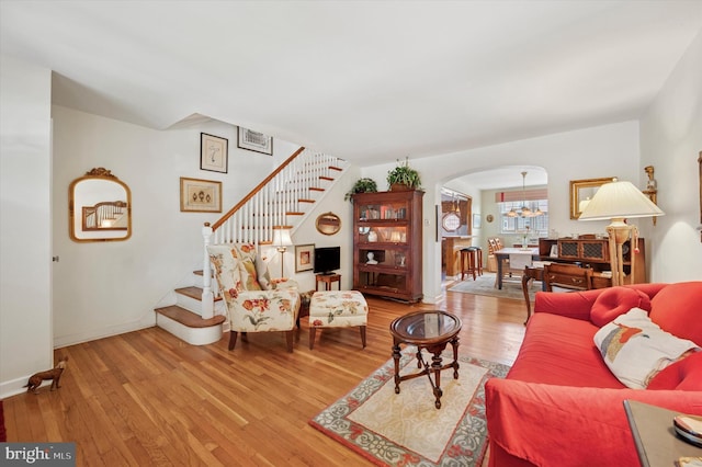 living area featuring arched walkways, hardwood / wood-style flooring, stairs, baseboards, and a chandelier