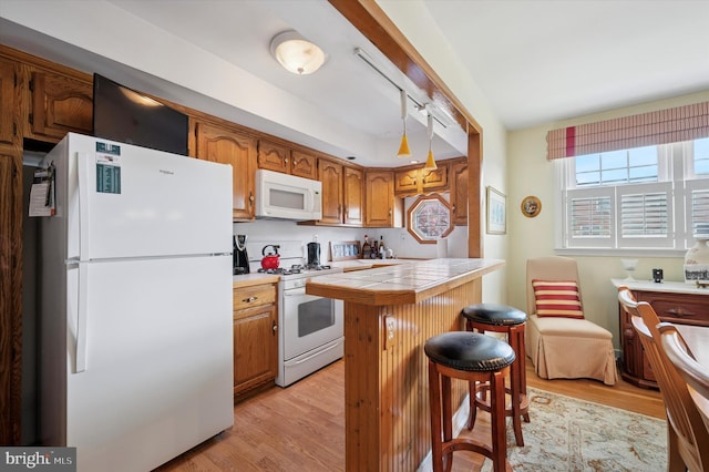 kitchen featuring white appliances, tile counters, a kitchen breakfast bar, light wood-type flooring, and brown cabinets