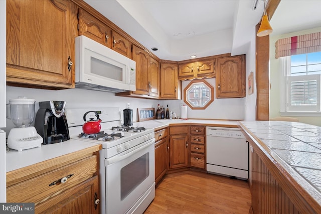 kitchen with white appliances, brown cabinets, light wood-type flooring, and a sink