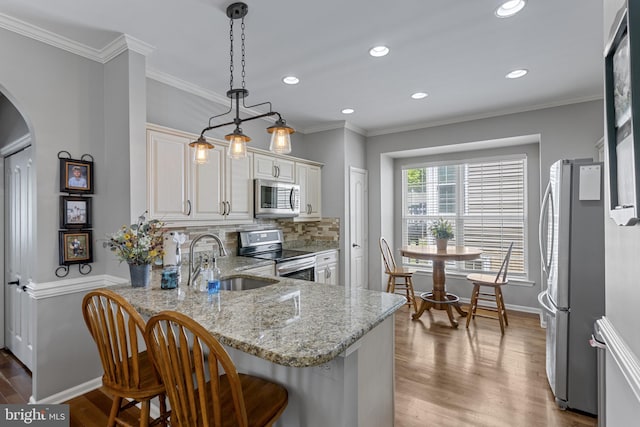 kitchen with stainless steel appliances, a sink, arched walkways, wood finished floors, and a peninsula