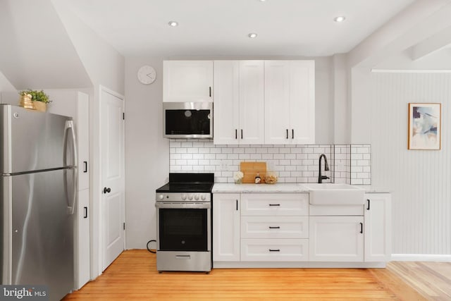 2420 2nd St NE, Washington, DC 20002 - kitchen featuring appliances with stainless steel finishes, light wood-type flooring, a sink, white cabinetry, and decorative backsplash