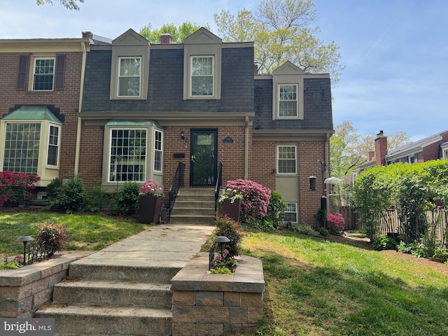 view of front of home with brick siding, a shingled roof, and mansard roof