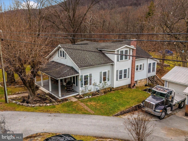view of front of house featuring roof with shingles, a porch, a front lawn, a chimney, and a garage