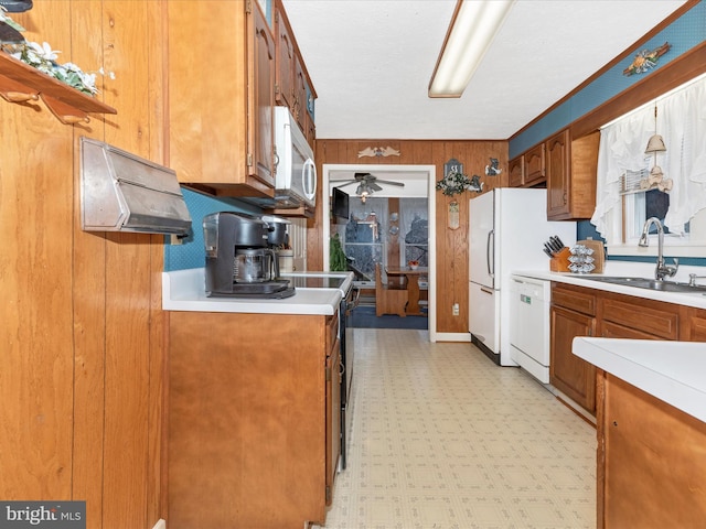kitchen with white appliances, a sink, light flooring, wood walls, and brown cabinetry