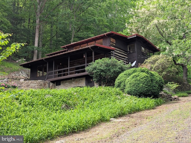 rear view of property with a view of trees, stone siding, and a balcony