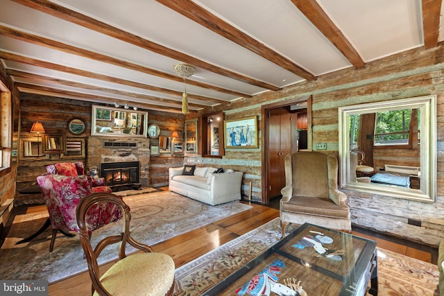 living area with a stone fireplace, beamed ceiling, and wood finished floors
