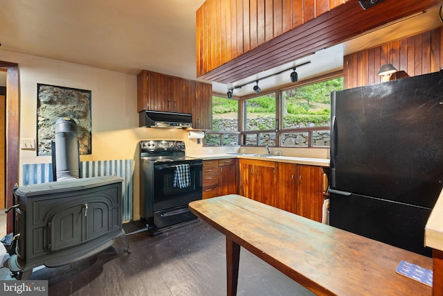 kitchen featuring black appliances, range hood, a wood stove, wood counters, and brown cabinets