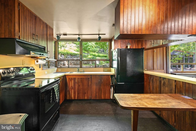kitchen with under cabinet range hood, black appliances, light countertops, finished concrete flooring, and wooden walls