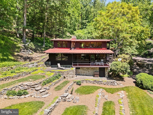 view of front of house with metal roof, a chimney, a standing seam roof, a forest view, and stone siding