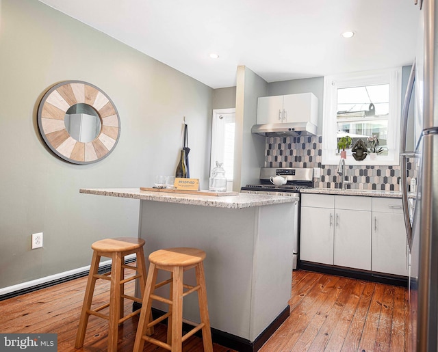 3211 Leverton Ave, Baltimore, MD 21224 - kitchen featuring gas stove, hardwood / wood-style floors, a breakfast bar area, white cabinets, and backsplash