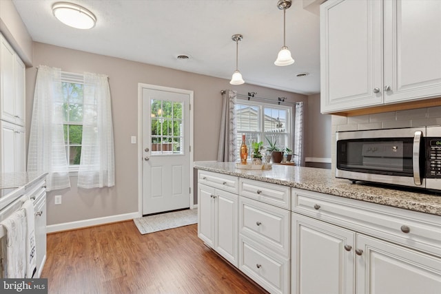 kitchen featuring stainless steel microwave, white cabinets, light wood-style flooring, baseboards, and pendant lighting