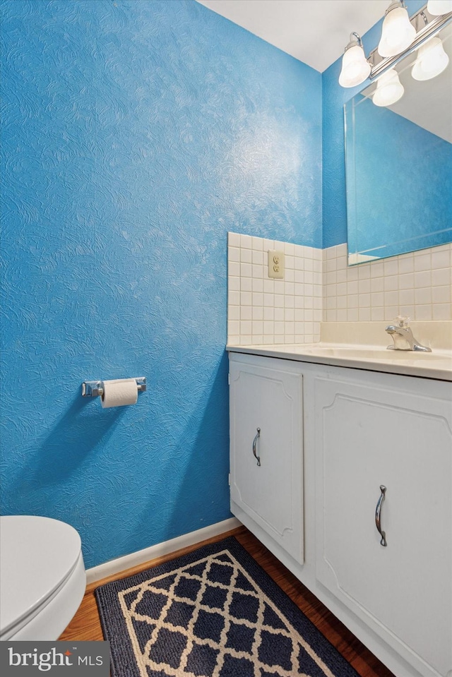 half bath with wood finished floors, toilet, baseboards, vanity, and decorative backsplash