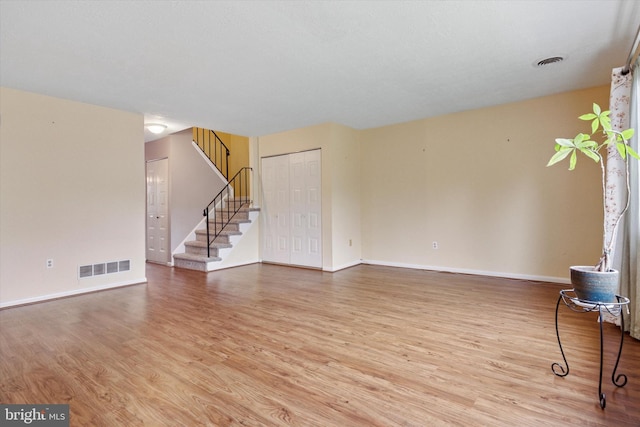 unfurnished living room featuring wood finished floors, stairway, and baseboards