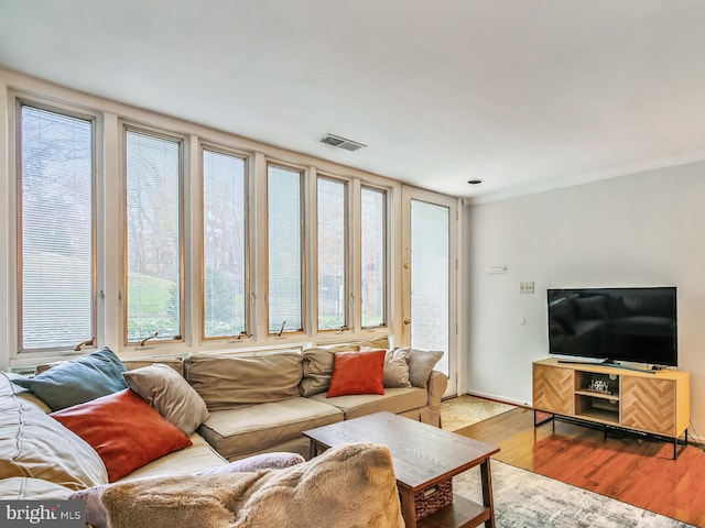 living area featuring healthy amount of natural light, wood finished floors, and ornamental molding