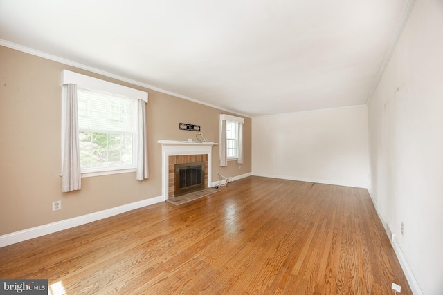 unfurnished living room with light wood-style flooring, ornamental molding, a brick fireplace, and baseboards