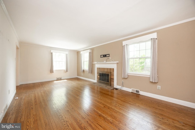 unfurnished living room with ornamental molding, wood finished floors, a tiled fireplace, and baseboards