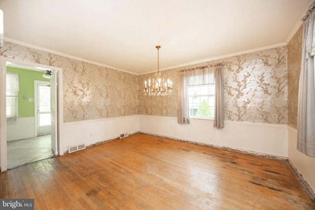 unfurnished dining area with a wainscoted wall, hardwood / wood-style floors, a chandelier, wallpapered walls, and ornamental molding