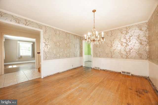 spare room with wainscoting, wallpapered walls, wood finished floors, a chandelier, and ornamental molding