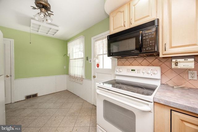 kitchen featuring black microwave, white range with electric stovetop, a wainscoted wall, light brown cabinets, and light countertops