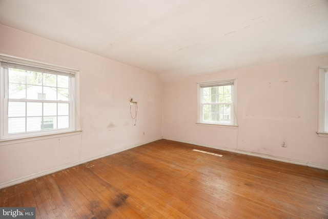 empty room with hardwood / wood-style flooring, baseboards, and lofted ceiling