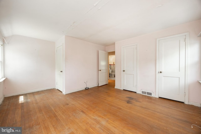unfurnished bedroom with light wood-type flooring, baseboards, and vaulted ceiling