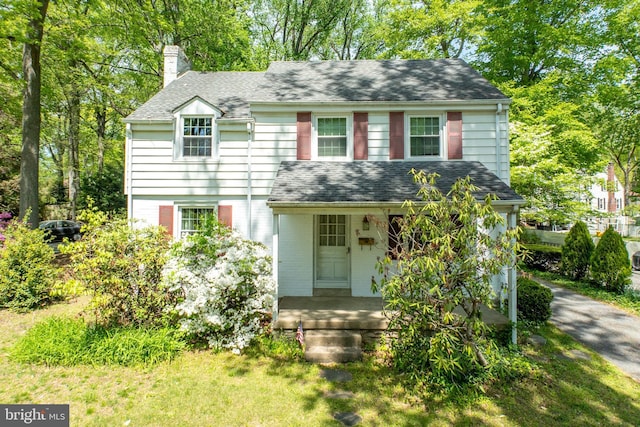 view of front facade featuring a porch, a chimney, and a shingled roof