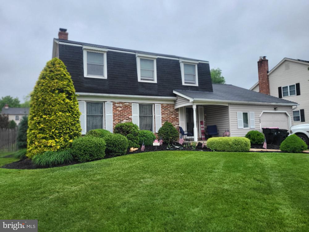 view of front of property with a front lawn, roof with shingles, a garage, mansard roof, and a chimney