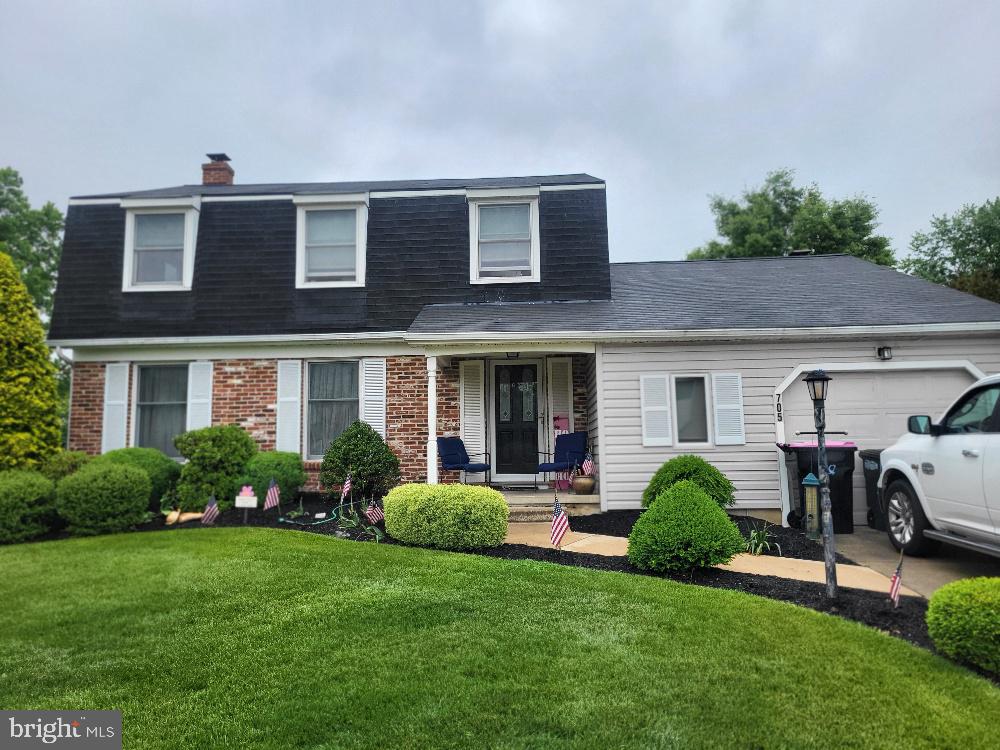 view of front of house with a shingled roof, mansard roof, a garage, a front lawn, and covered porch