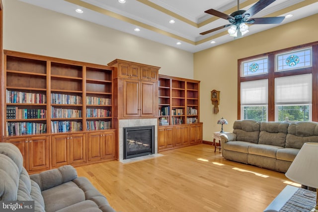 living area featuring a high ceiling, ceiling fan, light wood finished floors, a fireplace, and crown molding
