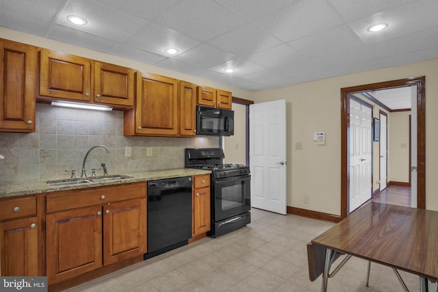 kitchen featuring black appliances, a sink, brown cabinets, tasteful backsplash, and light stone countertops