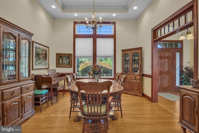 dining space with a chandelier, light wood finished floors, a high ceiling, crown molding, and a raised ceiling