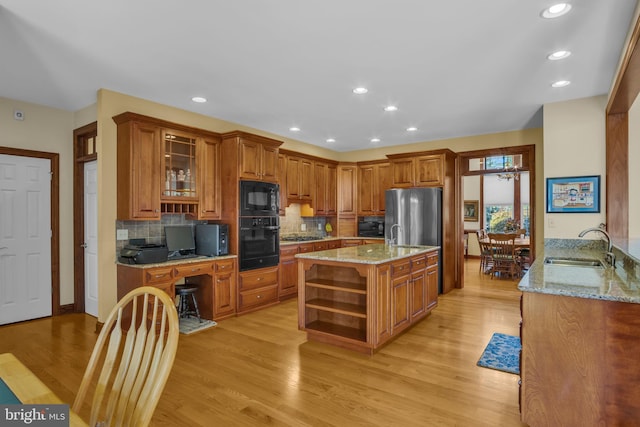 kitchen with black appliances, open shelves, a sink, brown cabinetry, and light stone countertops