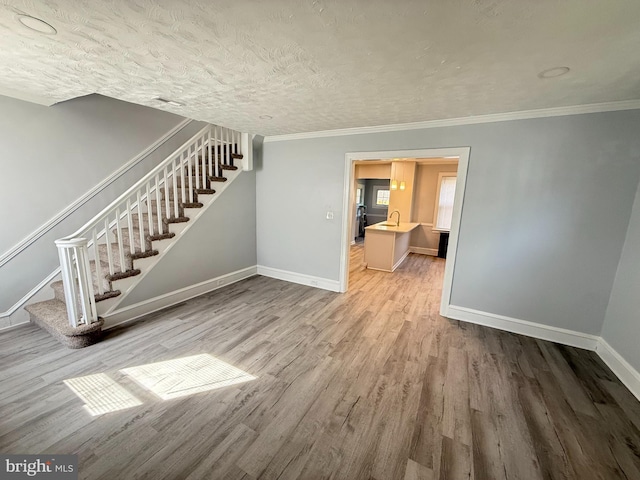 unfurnished living room featuring stairway, wood finished floors, baseboards, a sink, and ornamental molding