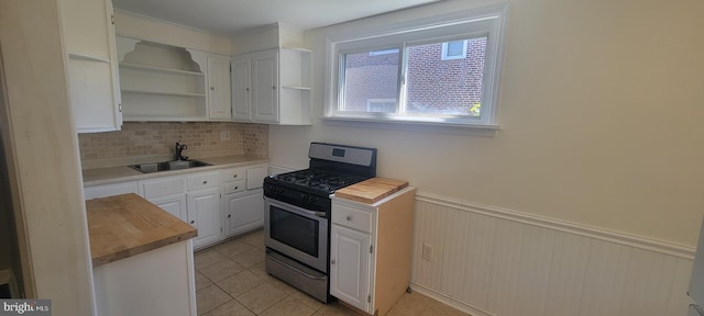 kitchen with stainless steel range with gas stovetop, a sink, wooden counters, tasteful backsplash, and white cabinetry