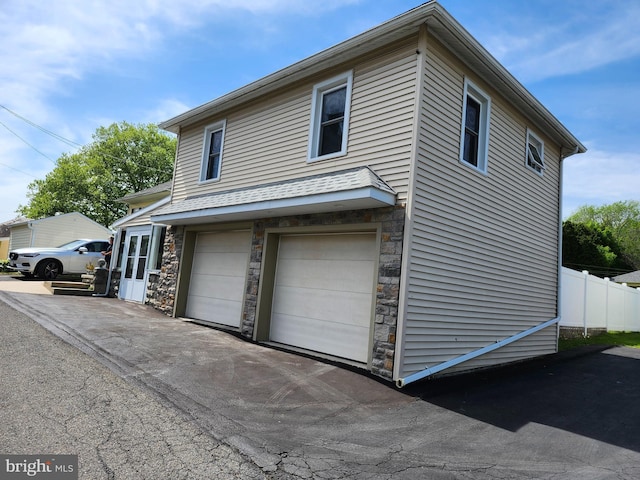 view of side of home featuring stone siding, a garage, and fence