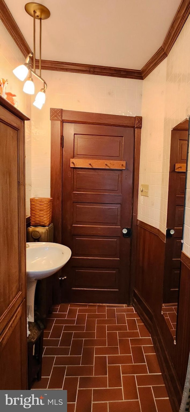 bathroom featuring crown molding, brick patterned floors, and a wainscoted wall