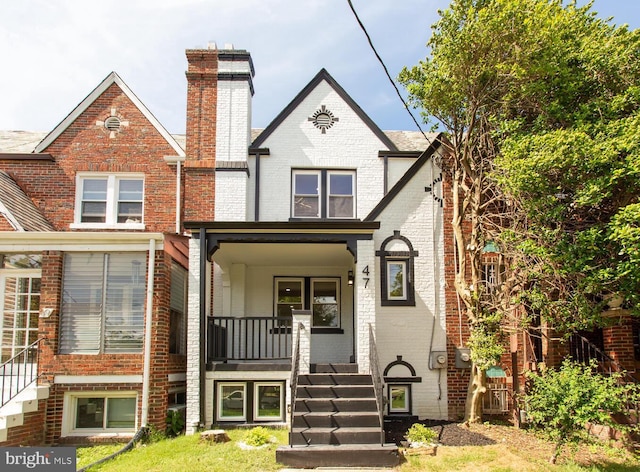 view of front of property featuring brick siding, a chimney, a porch, and stairway