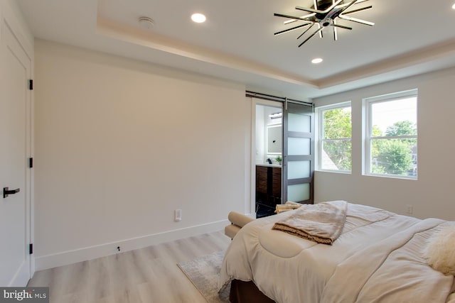 bedroom with a raised ceiling, light wood-type flooring, recessed lighting, baseboards, and a barn door