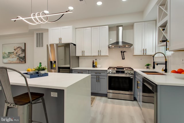 kitchen with stainless steel appliances, wall chimney range hood, a sink, gray cabinetry, and light countertops