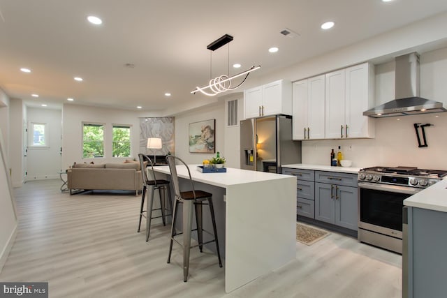 kitchen featuring wall chimney exhaust hood, stainless steel appliances, light wood-style flooring, light countertops, and a kitchen bar