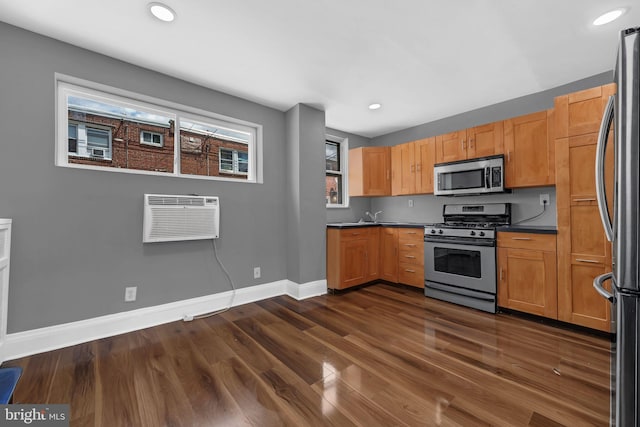 kitchen featuring stainless steel appliances, a wall mounted air conditioner, baseboards, dark countertops, and dark wood finished floors