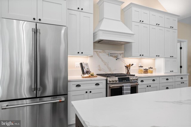5570 Warren Dr, Huntingtown, MD 20639 - kitchen featuring appliances with stainless steel finishes, premium range hood, white cabinetry, decorative backsplash, and light stone counters