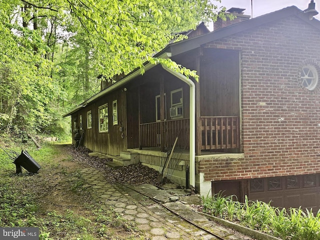 view of home's exterior featuring brick siding, a garage, cooling unit, and a chimney