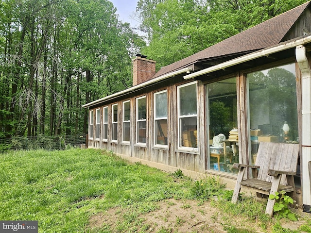 view of home's exterior featuring a chimney, a shingled roof, a sunroom, and fence