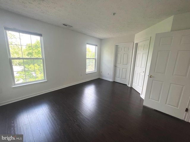 unfurnished bedroom with baseboards, multiple windows, dark wood-style floors, and a textured ceiling