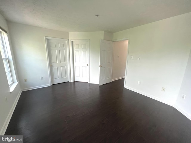 unfurnished bedroom with dark wood-style flooring, baseboards, and a closet